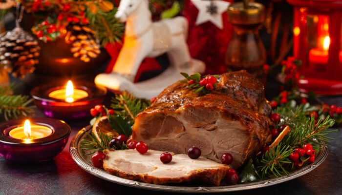 Roast pork neck in Christmas style Dark navy blue background Christmas accessories Candles and lanterns in the background 