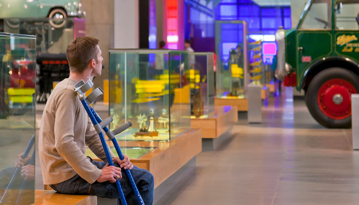 Person sitting down looking at the displays in a museum holding their crutches