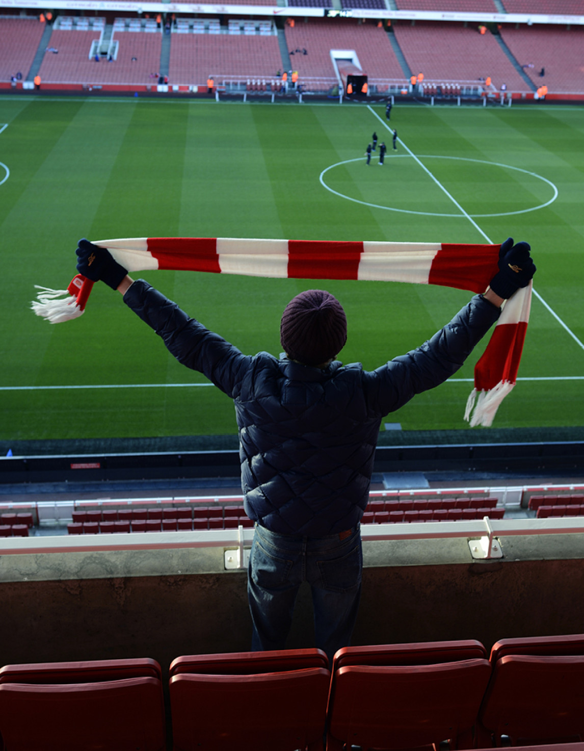 Man holding up a football scarf facing a football pitch